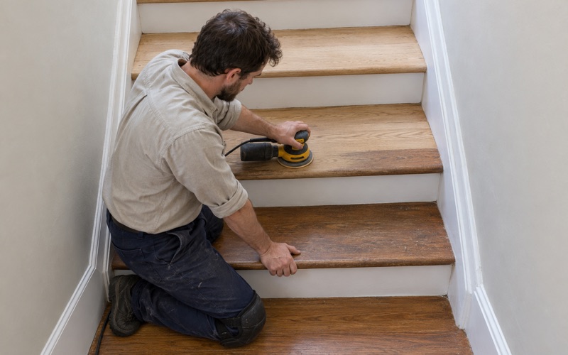 Worker sanding the oak treads of the shared front stair in a Somerville three-decker, the risers left painted.